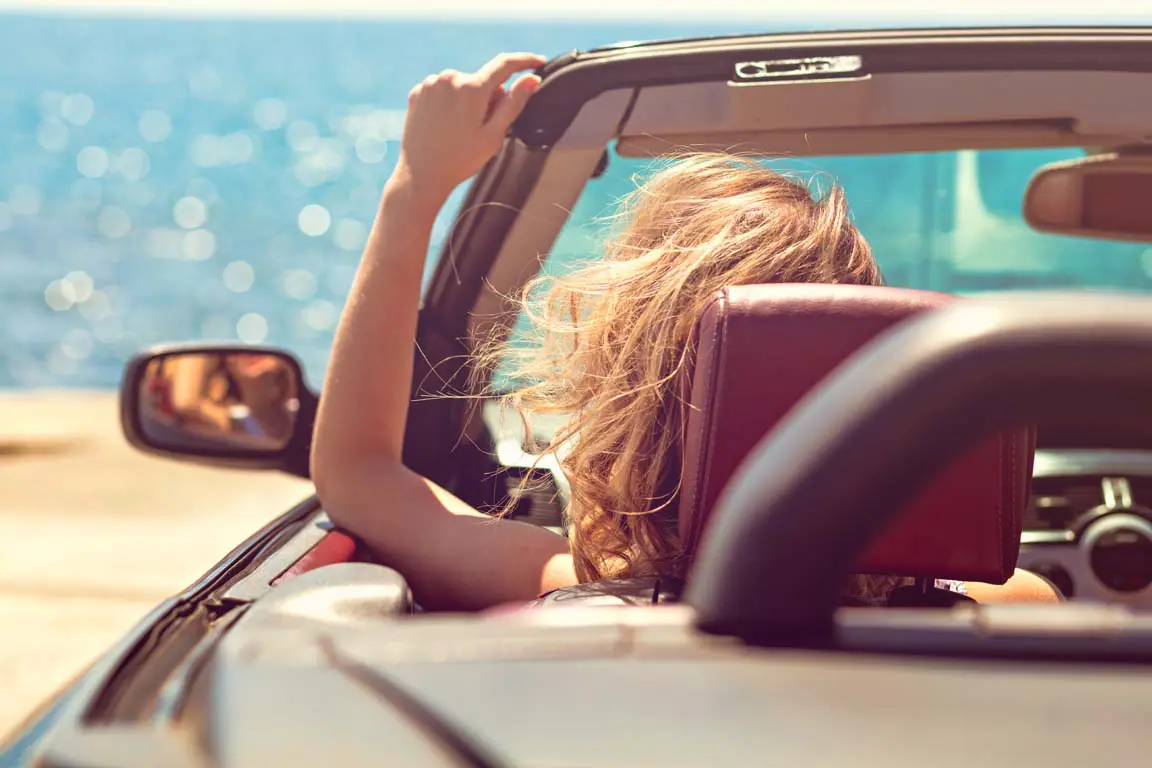 woman in car with top down convertible driving to the beach