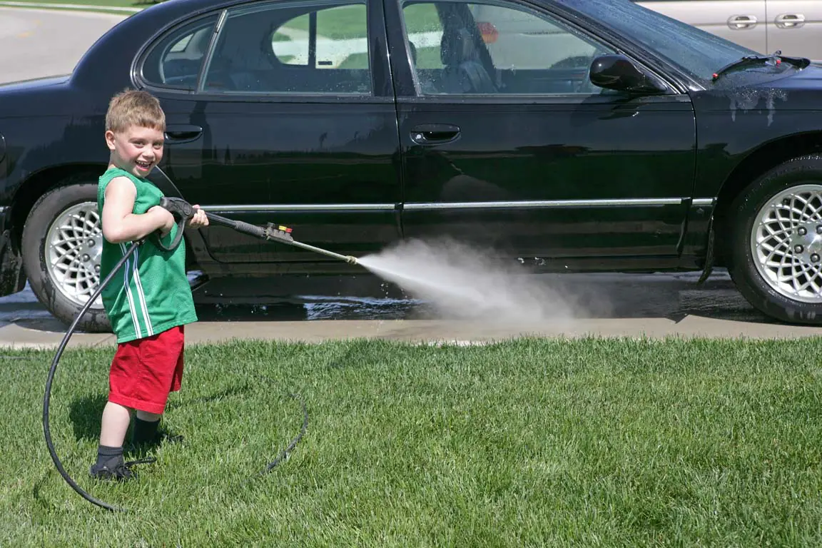 young boy power washing a black car in his driveway instead of going to a local car wash